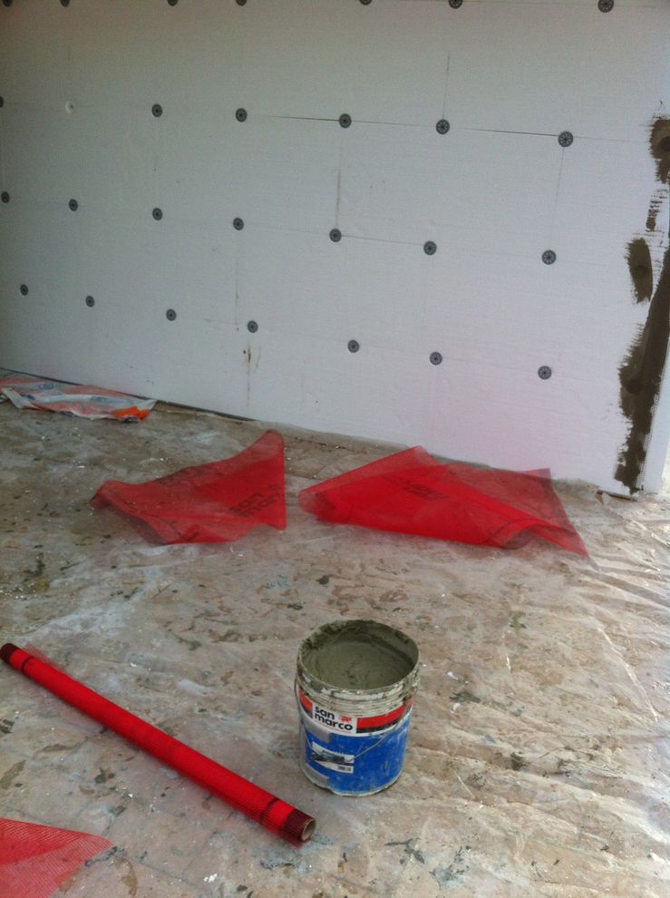 Pavimento da cantiere con attrezzi rossi, una bomboletta di adesivo e un pannello parzialmente installato con fori delle viti visibili.