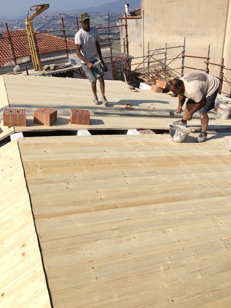 Operai edili posano pannelli di compensato su una terrazza sul tetto, con la città e le montagne sullo sfondo.