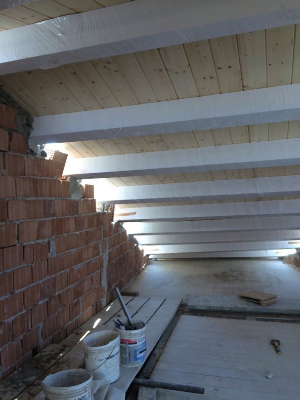 Interno della soffitta con travi a vista, muro in mattoni e secchi da cantiere sul pavimento.