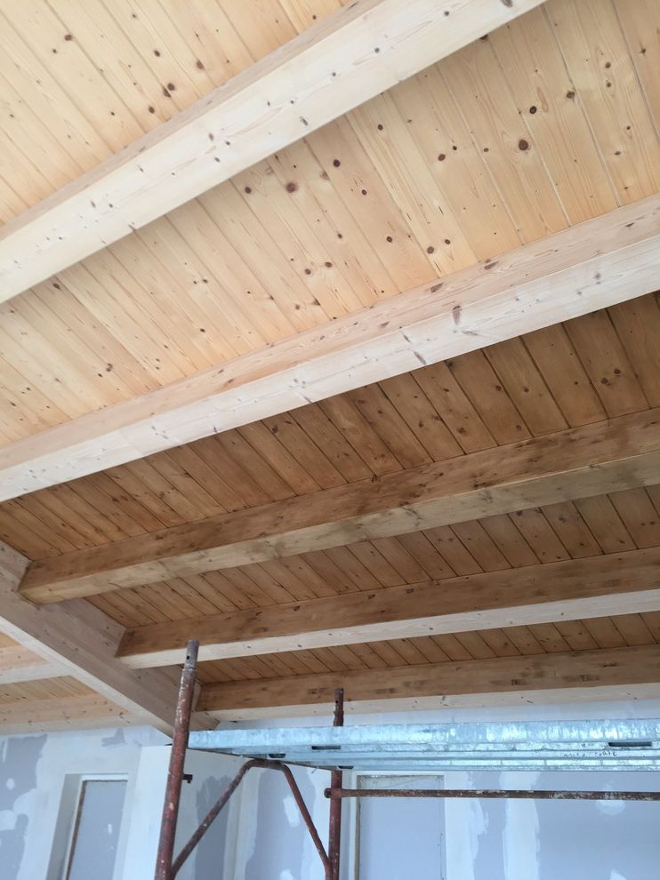 Travi in ​​legno a vista sul soffitto in un interno non rifinito con impalcature e un'apertura di porta sottostante.