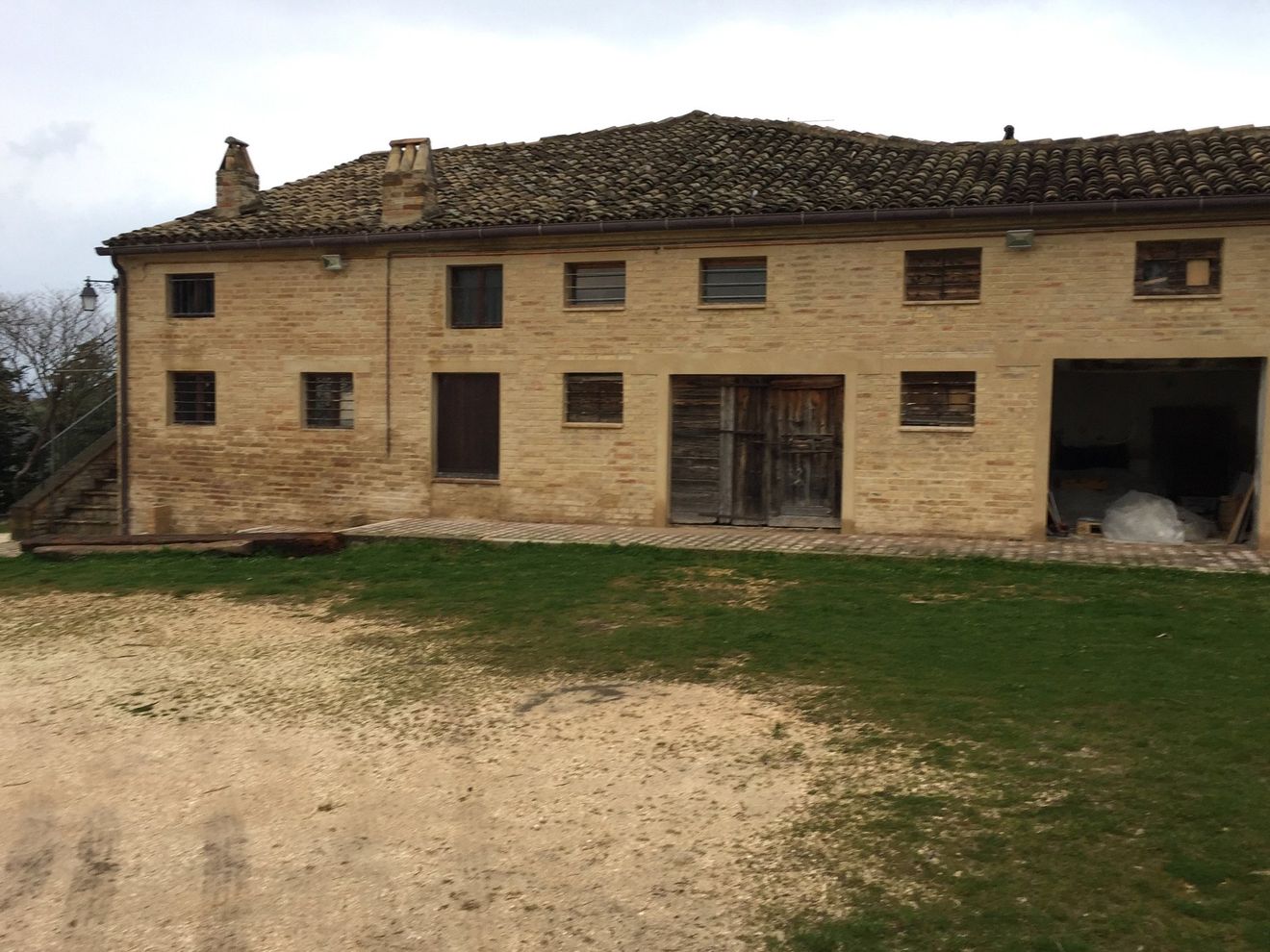 Antica casa colonica in pietra con tetto di tegole, piccole finestre e porta di accesso aperta in un cortile erboso.