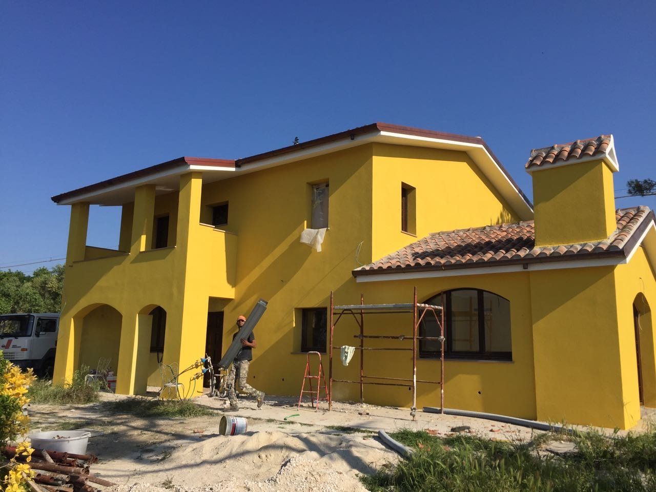 Casa gialla a due piani con tetto in terracotta e cortile anteriore non rifinito, attualmente in costruzione.