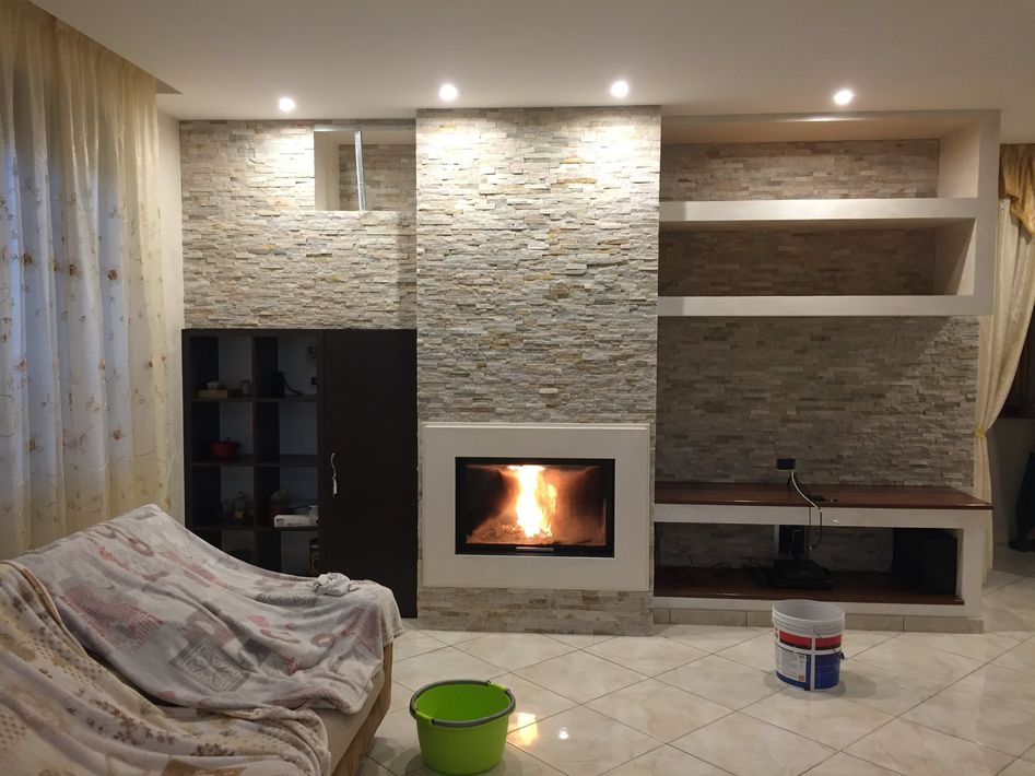 Accogliente soggiorno con camino in pietra, scaffali a muro e divano, illuminato da calde luci a incasso.