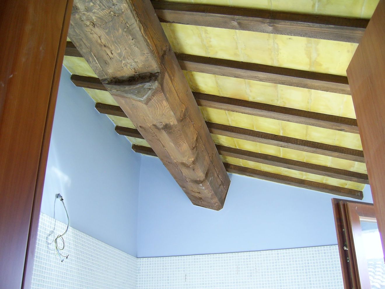 Soffitto interno con travi in ​​legno a vista e pannelli traslucidi gialli sopra pareti piastrellate