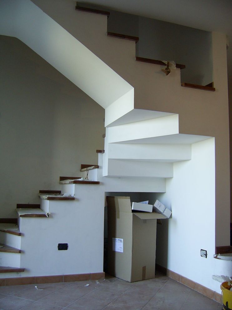 Scala interna con pareti bianche, gradini in legno scuro e una piccola porta sotto le scale