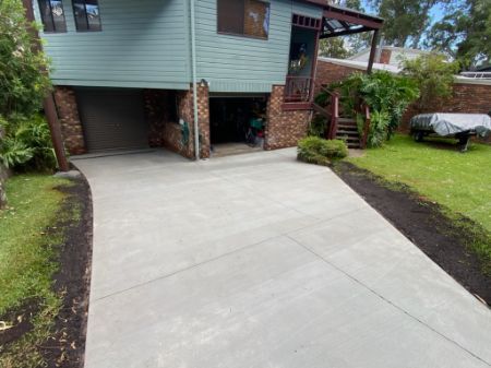 A Concrete Driveway Leading to a House With a Garage — Jaya Rose Earthworks and Landscape Contractors In Gulmarrad, NSW
