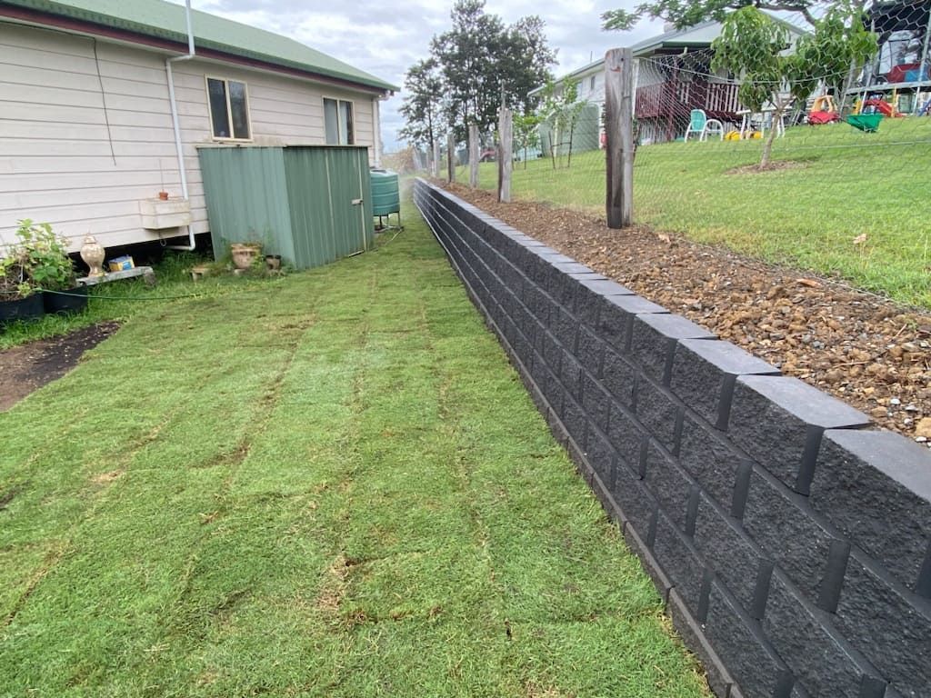 A Brick Wall Surrounds a Lush Green Lawn  — Jaya Rose Earthworks and Landscape Contractors In Gulmarrad, NSW