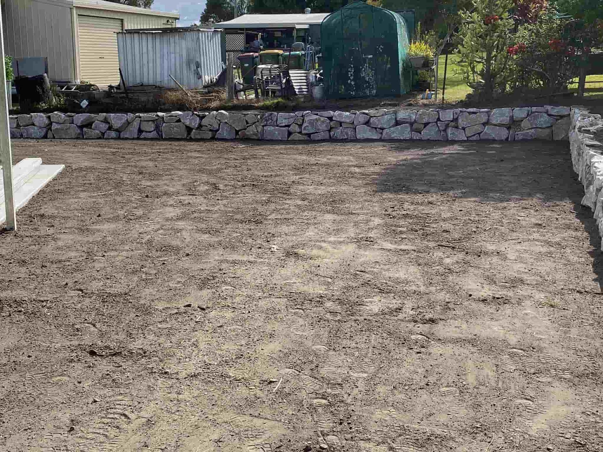 A Dirt Field With a Stone Wall — Jaya Rose Earthworks and Landscape Contractors In Iluka, NSW