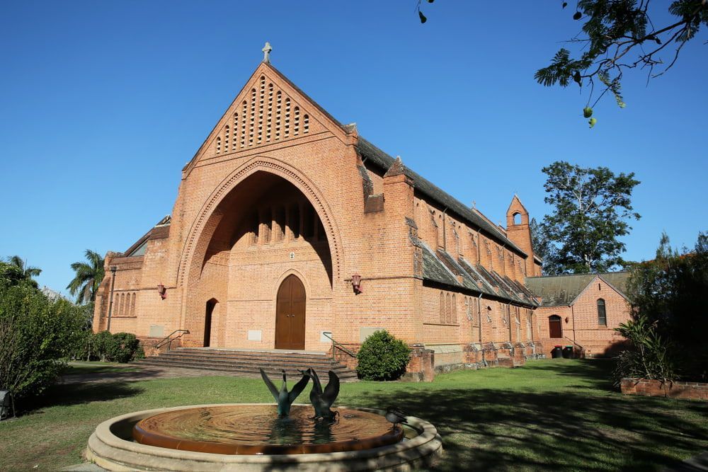 A Large Brick Church With a Fountain in Front of It — Jaya Rose Earthworks and Landscape Contractors In Grafton, NSW