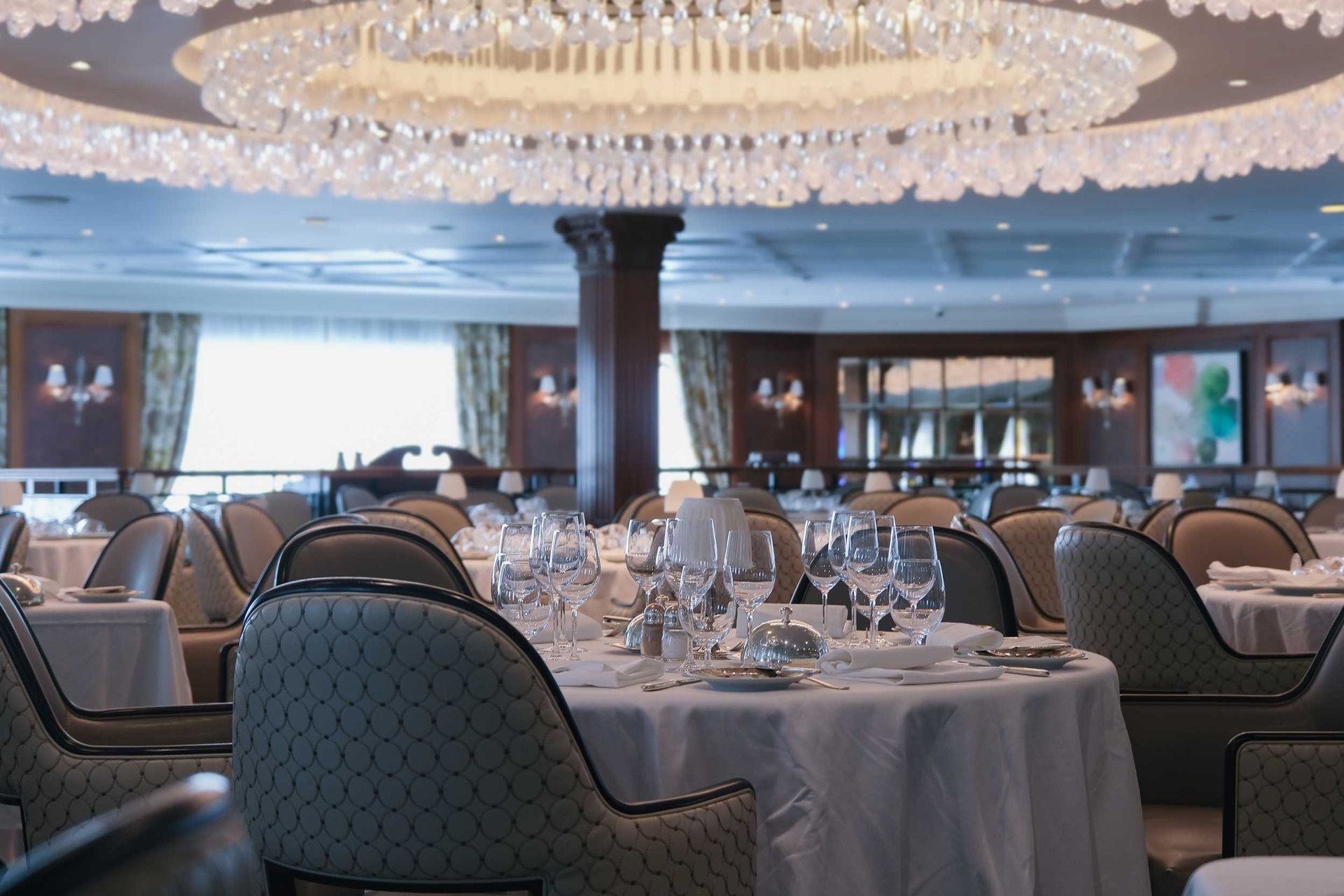 Country club dining room with crystal chandelier and formally set tables. Country club dining room with crystal chandelier and formally set tables.