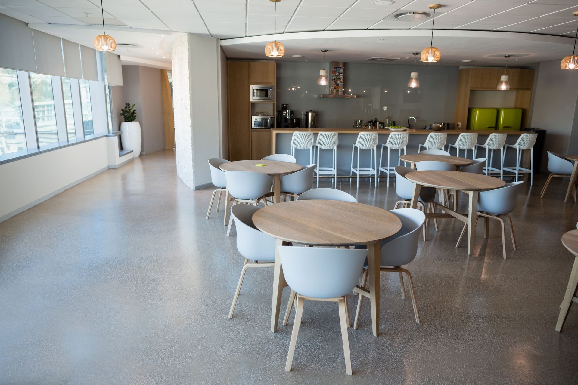 Empty modern office break room with tables, chairs, and a kitchen with bar stools.