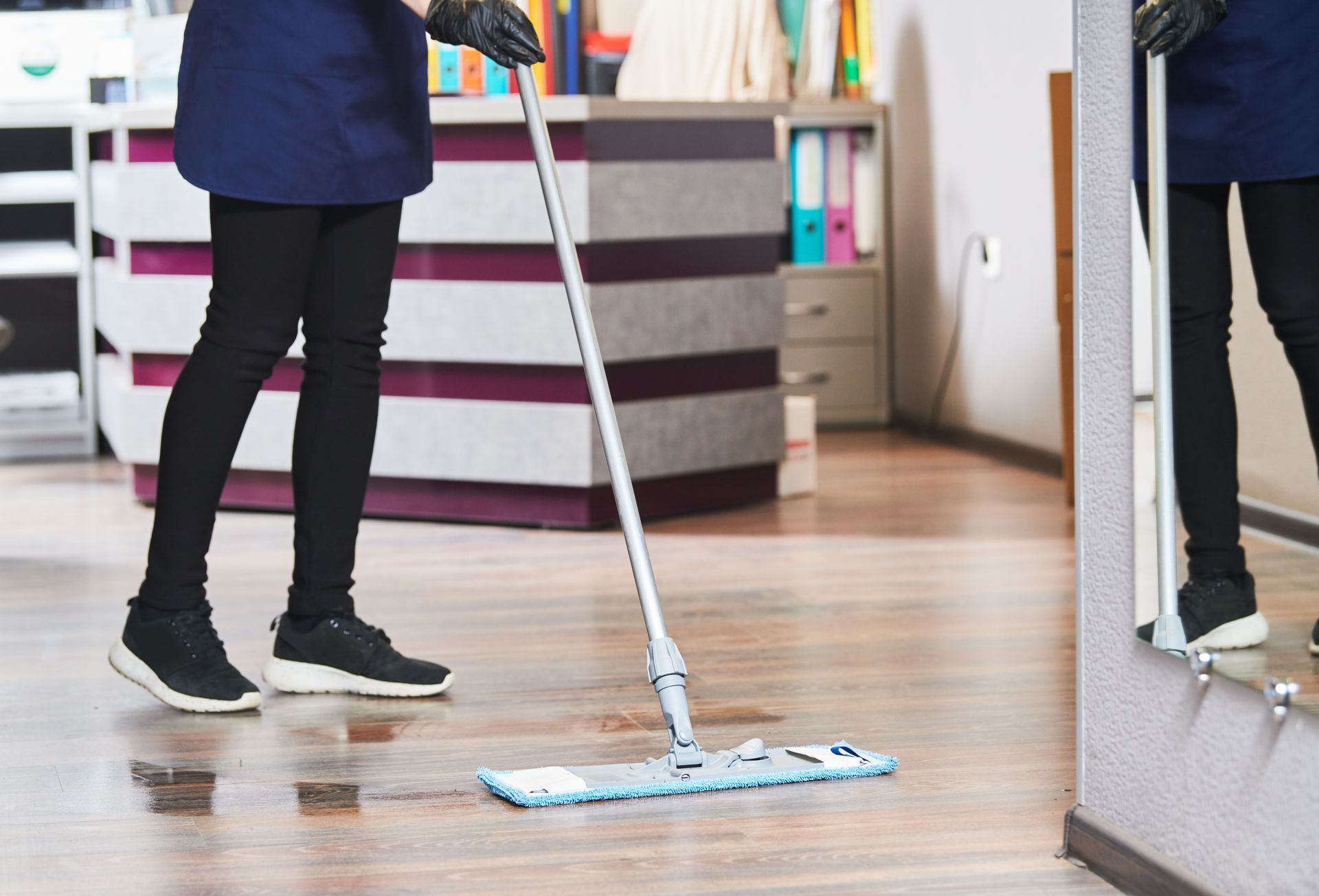 Person mopping a wood floor in a room with a mirror and striped counter.