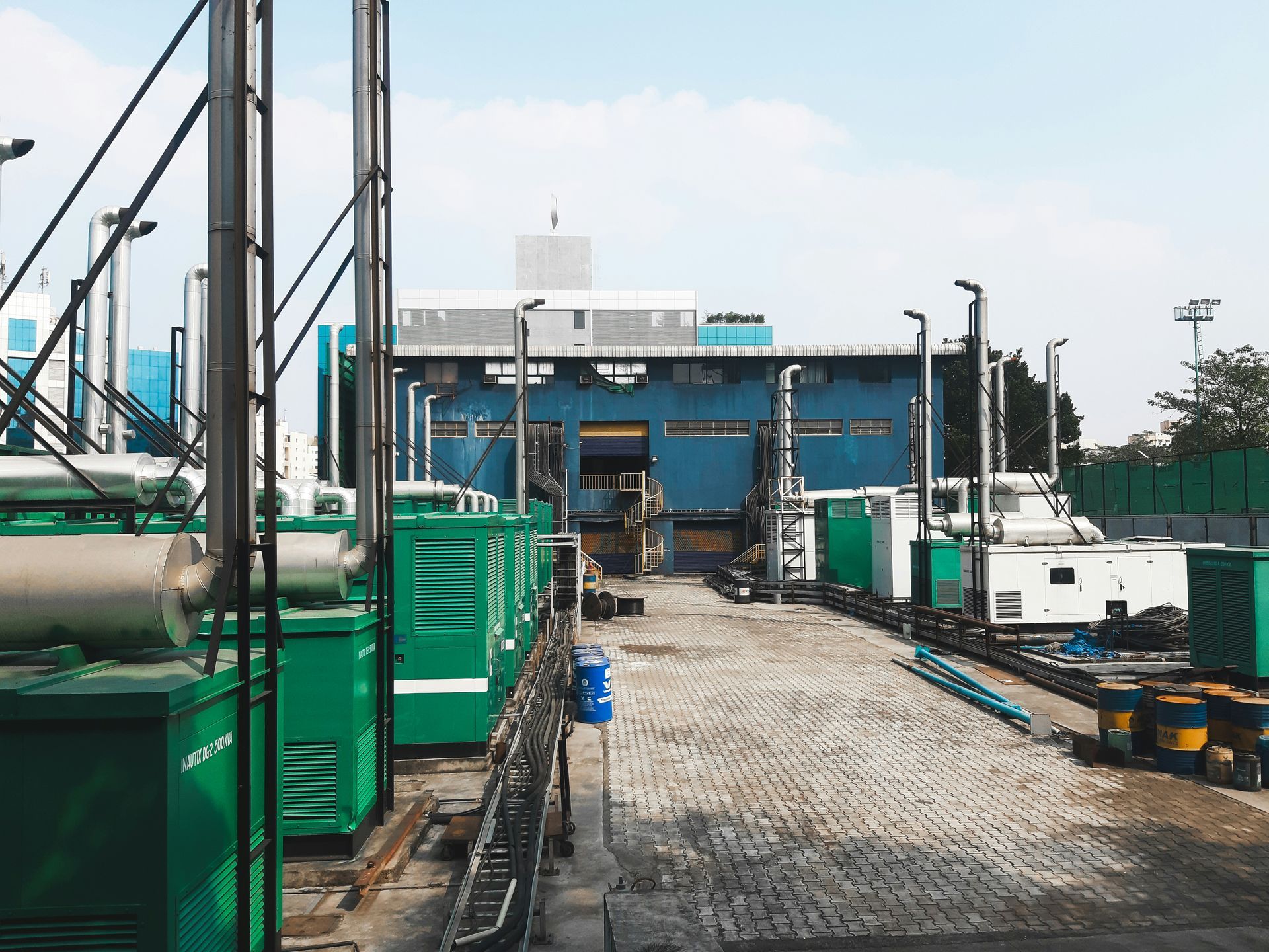 Vue extérieure d'une centrale électrique avec des générateurs verts, un bâtiment bleu et un chemin pavé.
