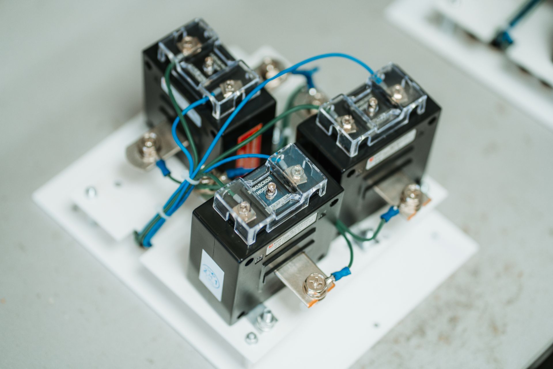 Trois composants électriques noirs câblés ensemble sur une base blanche, avec des fils bleus et verts.