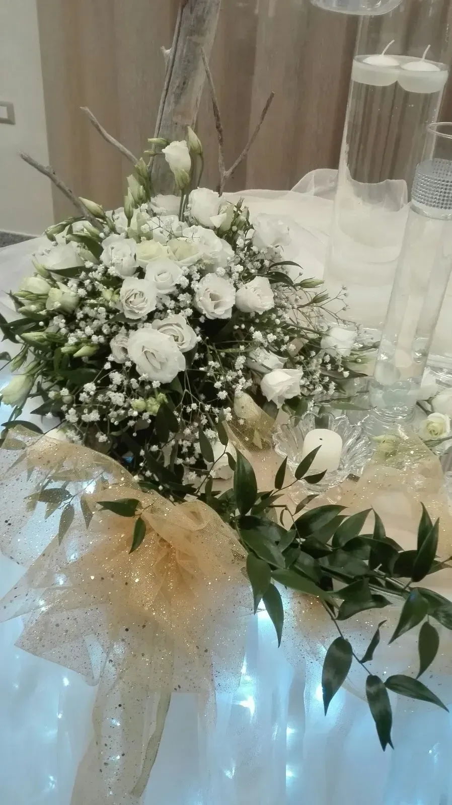 Bouquet di fiori bianchi con gypsophila e verde, disposto accanto a vasi di vetro alti con luci blu soffuse.
