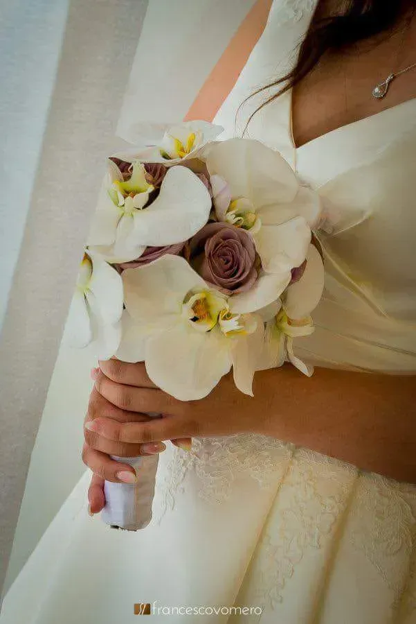 Sposa con abito color crema che tiene in mano un bouquet da sposa bianco e lavanda.