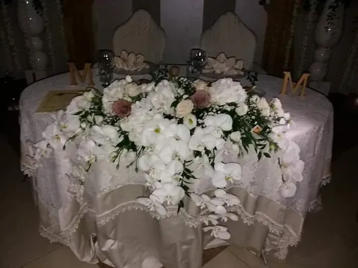 Composizione floreale bianca su un tavolo ricoperto di pizzo con lettere decorative e candele in una stanza scarsamente illuminata