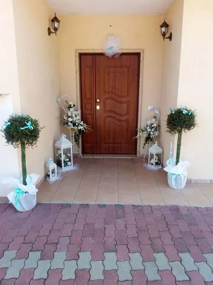 Ingresso decorato con doppie porte in legno, piante in vaso e lanterne lungo un portico piastrellato.