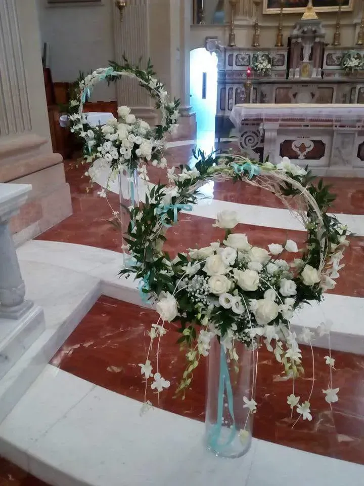 Composizioni floreali bianche a forma di cuore all'interno di una chiesa, su un pavimento di marmo rosso.