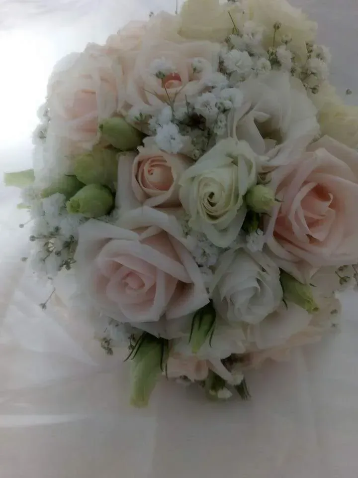 Bouquet di rose rosa tenue e bianche con gypsophila e boccioli verde pallido su sfondo bianco.