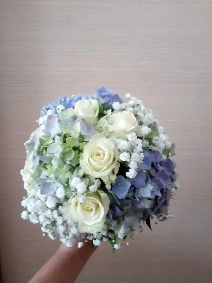 Bouquet di rose bianche e fiori azzurri su sfondo neutro, tenuto a mano.