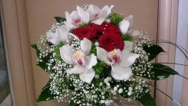 Bouquet di rose rosse e gigli bianchi con gypsophila, disposto su uno sfondo beige per interni.