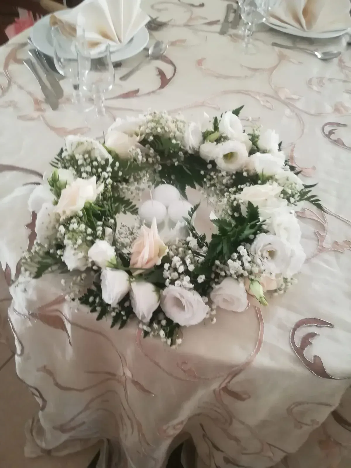 Centrotavola con ghirlanda di fiori bianchi su una tovaglia a fantasia, con tovaglioli piegati sullo sfondo.