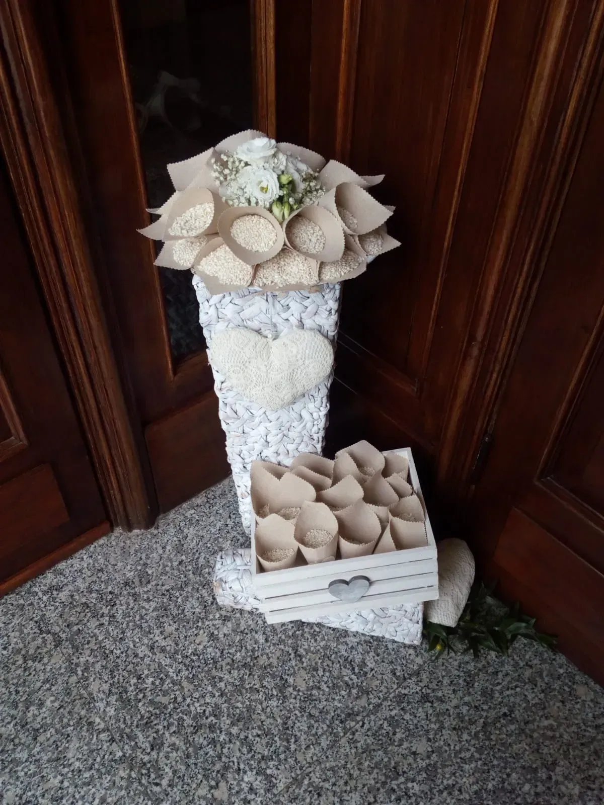 Composizione floreale di conchiglie bianche su un piedistallo accanto a una scatola di conchiglie, sullo sfondo di una porta di legno e un tappeto.