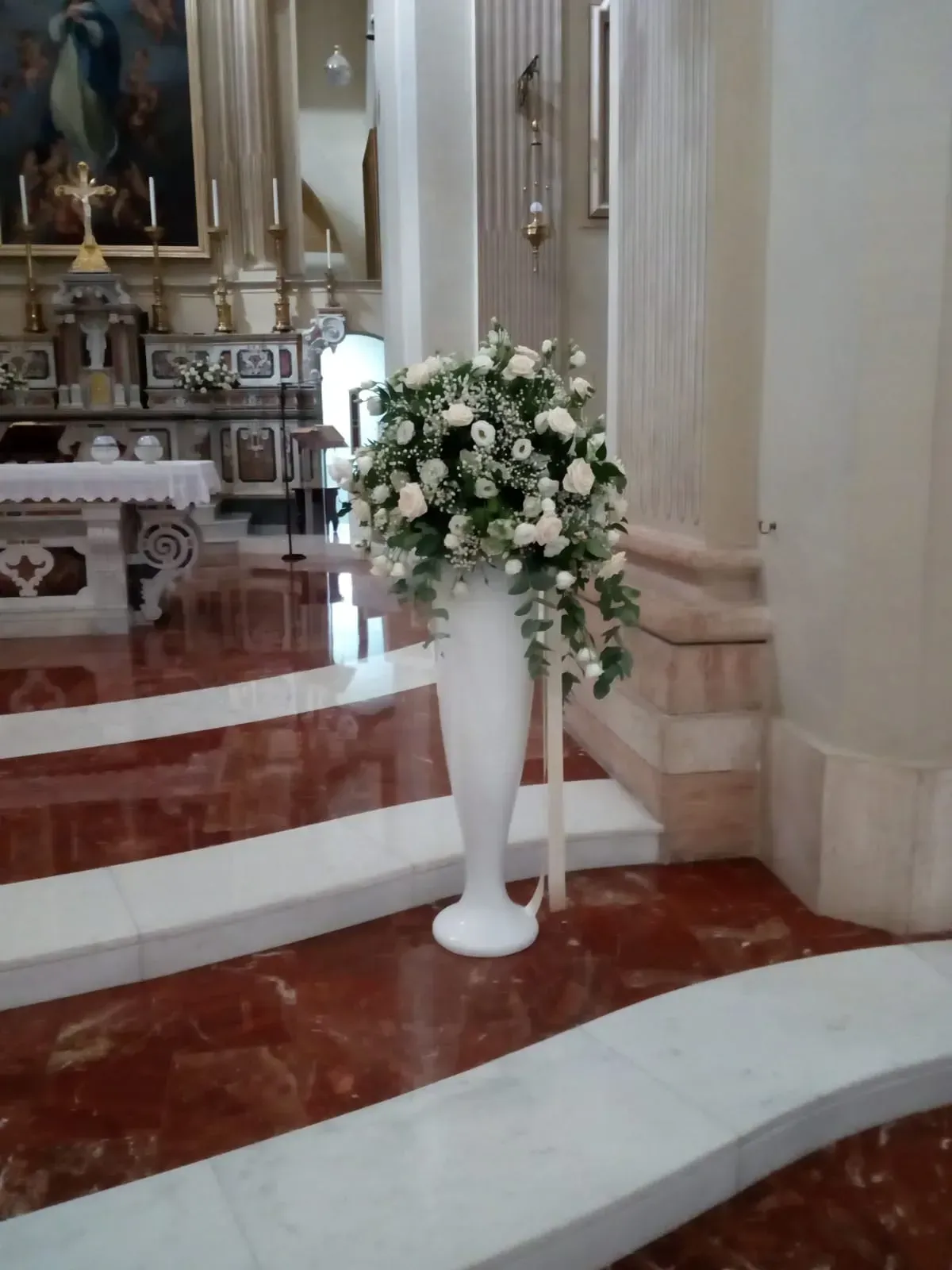 Composizione floreale bianca in un vaso alto accanto ai gradini della chiesa e all'area dell'altare.