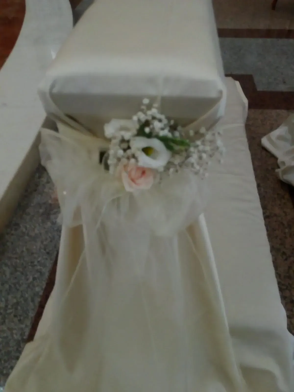 Sedia bianca con fascia color crema e piccolo bouquet floreale decorativo su un pavimento ricoperto di moquette.