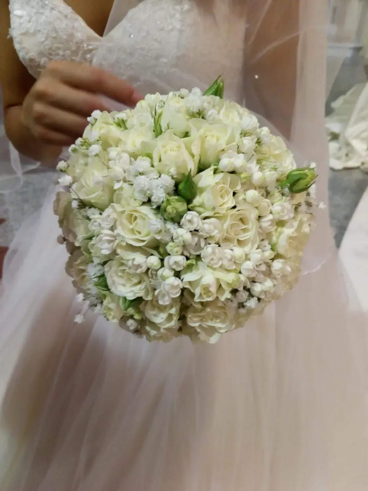 La sposa tiene in mano un bouquet rotondo di fiori bianchi con dettagli verdi, su un abito rosa tenue.