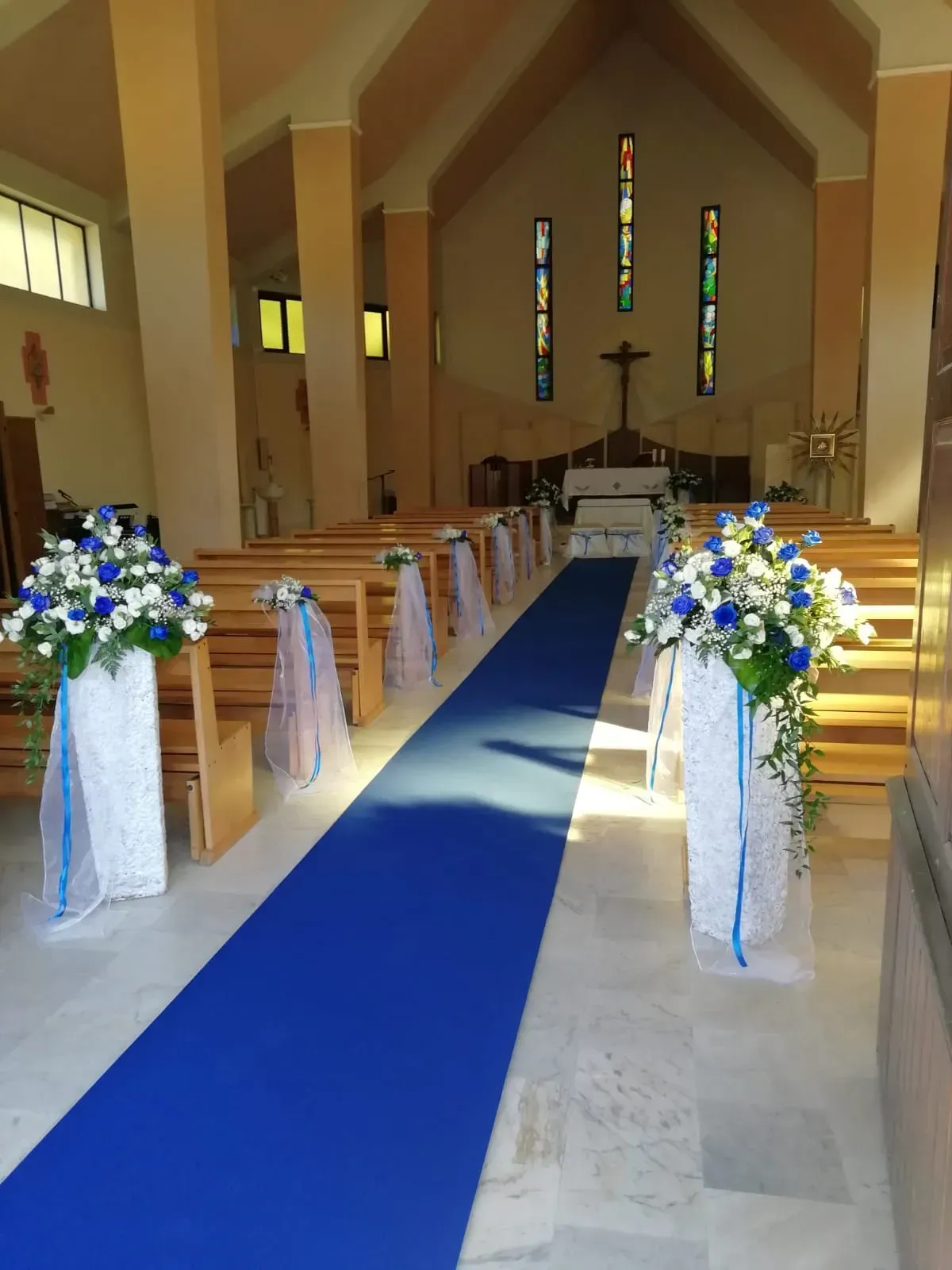 Navata della chiesa decorata con tappeto blu, composizioni floreali bianche e banchi che conducono all'altare