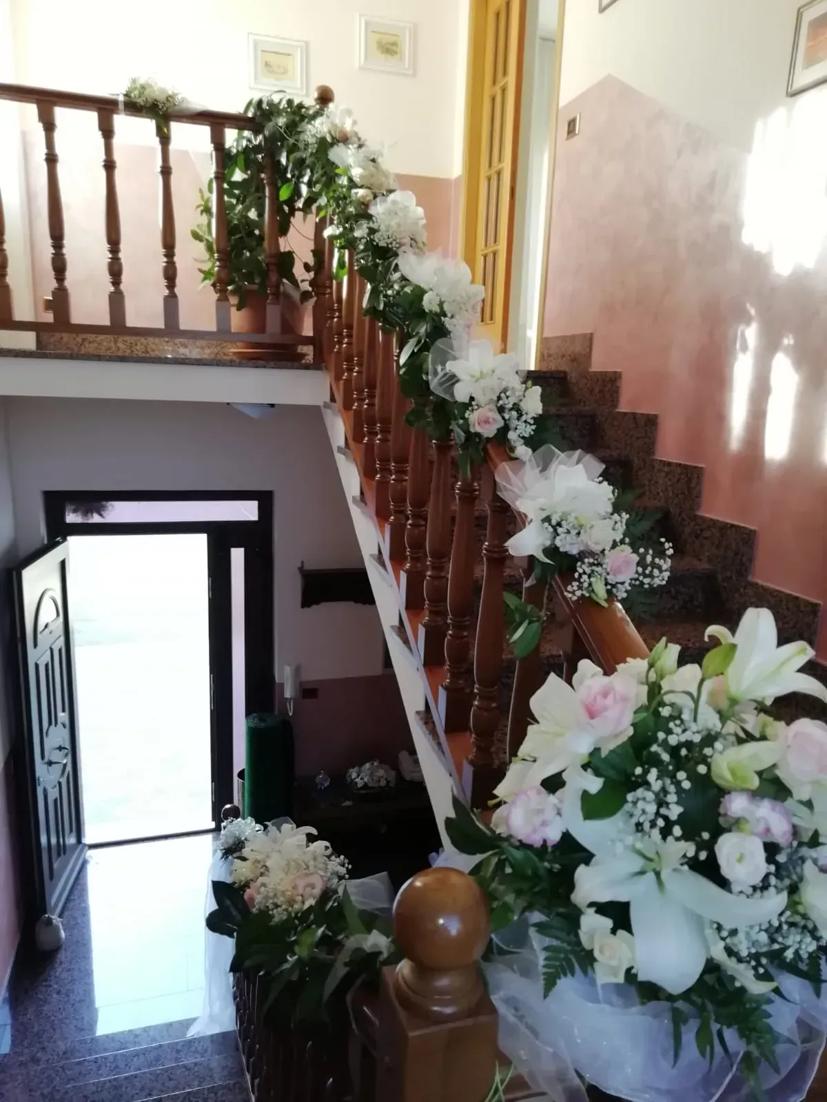 Scala e ringhiera decorate con fiori in un luminoso corridoio interno.