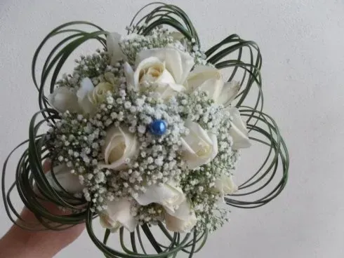 Bouquet di fiori bianchi con gypsophila, rose color crema e foglie verde scuro a forma di riccio.