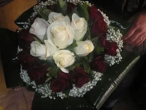 Un bouquet di rose bianche e bordeaux con gypsophila su una sedia scura, con una mano visibile accanto.