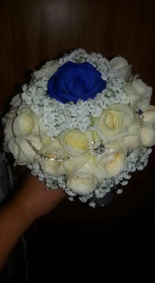 Bouquet di fiori bianchi con una singola rosa blu al centro, tenuto in mano su uno sfondo scuro.
