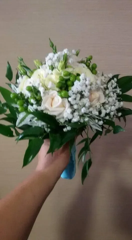 Una mano che regge un mazzo di fiori bianchi e verdi contro uno sfondo beige.