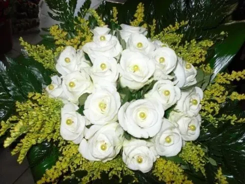 Rose bianche disposte in un bouquet con fiori di riempimento gialli e fogliame verde.