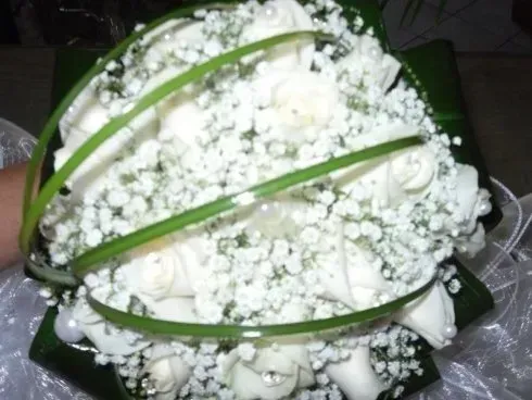 Bouquet di fiori bianchi con foglie verdi, disposti in un fitto mazzo su sfondo scuro.