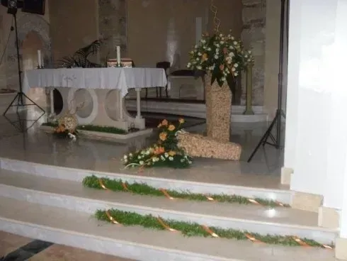 Altare della chiesa decorato con fiori bianchi e arancioni, candele e ghirlande verdi sui gradini