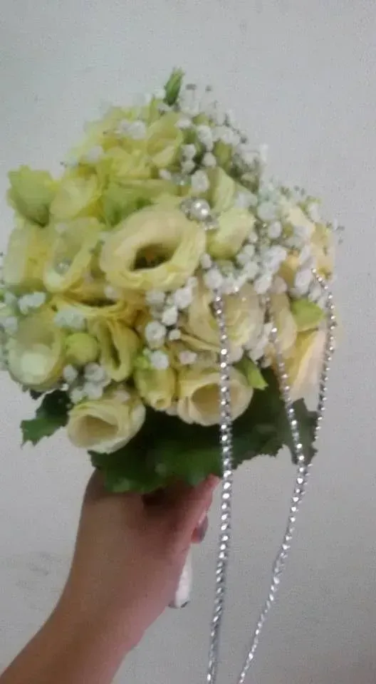 Mano che regge un mazzo di fiori giallo pallido e bianchi con fili di perline simili a perle.