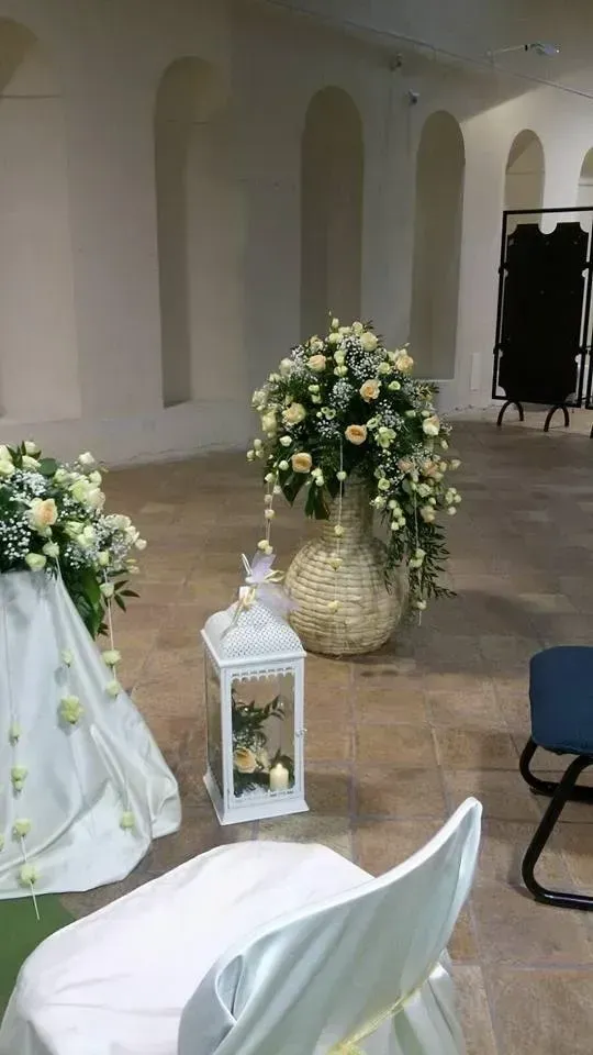 Navata nuziale con coprisedie bianchi, decorazioni con lanterne e grandi composizioni floreali bianche e gialle in una sala