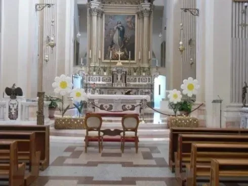 Altare della chiesa riccamente decorato con composizioni floreali bianche e banchi di legno in primo piano.