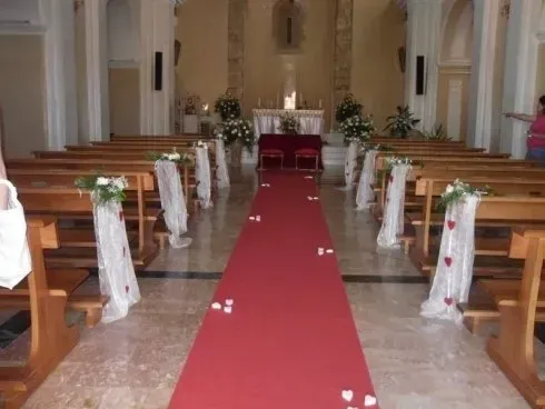 Navata della chiesa decorata con tappeto rosso, fiocchi bianchi e altare in fondo