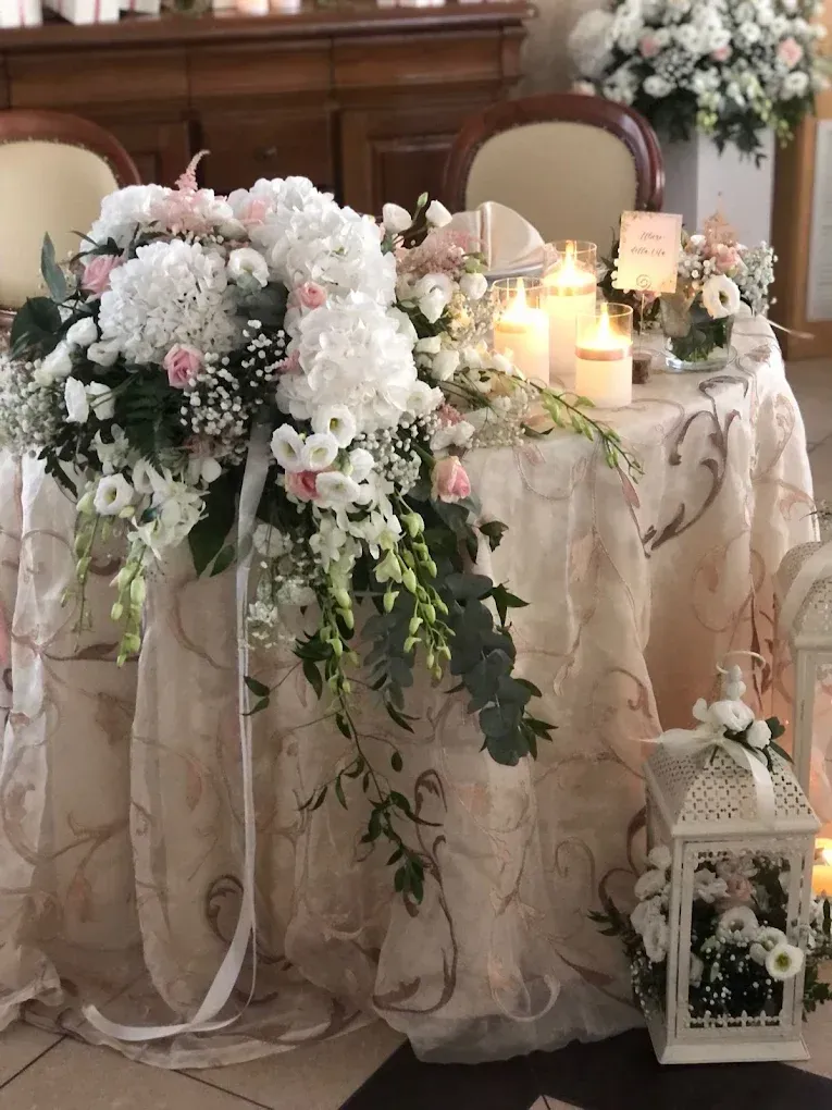 Tavolo decorato con fiori bianchi, candele e una lanterna in una delicata atmosfera da ricevimento di nozze.