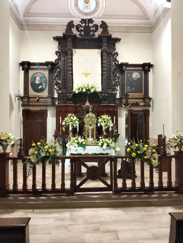 Altare ecclesiastico riccamente decorato con composizioni floreali, candele e ritratti incorniciati in una cappella a volta.