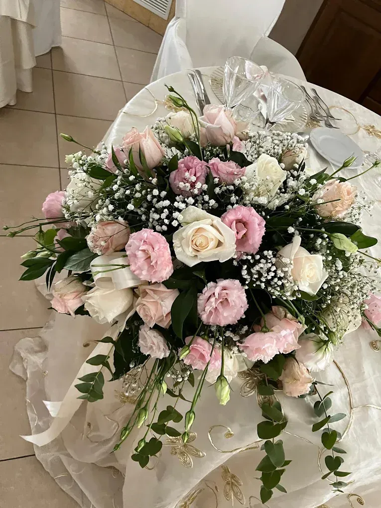 Composizione floreale rosa e bianca con rose e gypsophila su un supporto bianco drappeggiato.