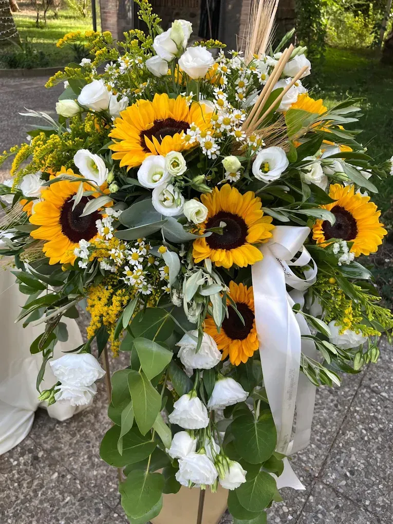 Composizione floreale di girasoli e rose bianche con fogliame verde e nastro bianco, da esterno.