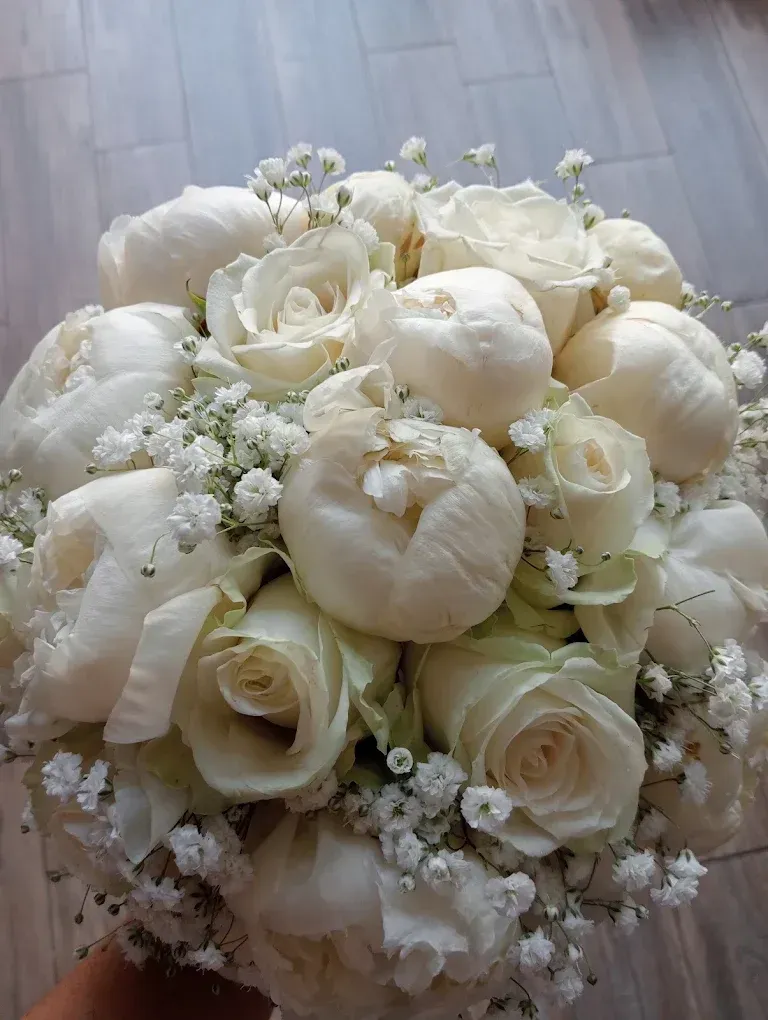 Bouquet da sposa bianco di rose e gypsophila su una base di legno chiaro.