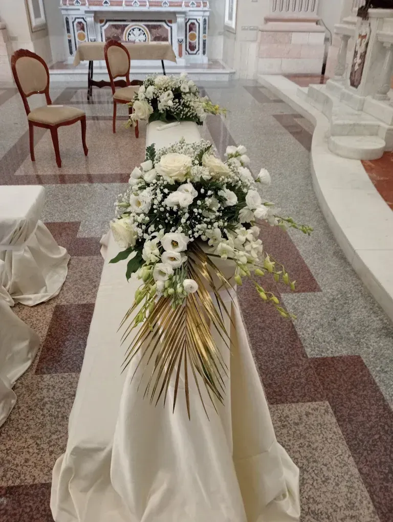 Composizione floreale bianca lungo la navata, con verde drappeggiato su un piedistallo anch'esso drappeggiato, all'interno di una chiesa.